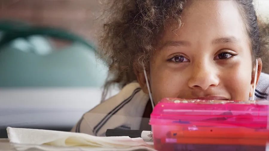 A young girl smiles from behind her pencil case.
