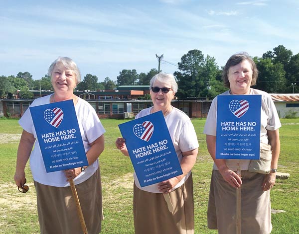 Three sisters hold signs saying "Hate has no home here."
